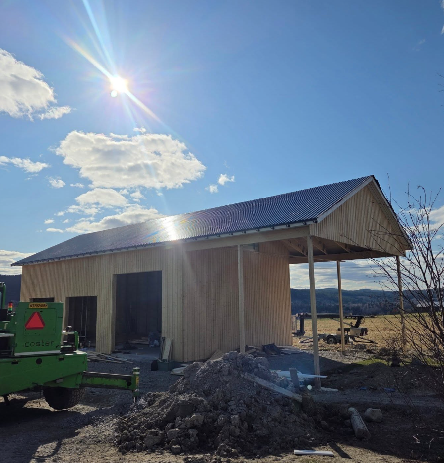 Färdigt garage med bandat plåttak, stående träpanel och skärmtak med carport i solsken.